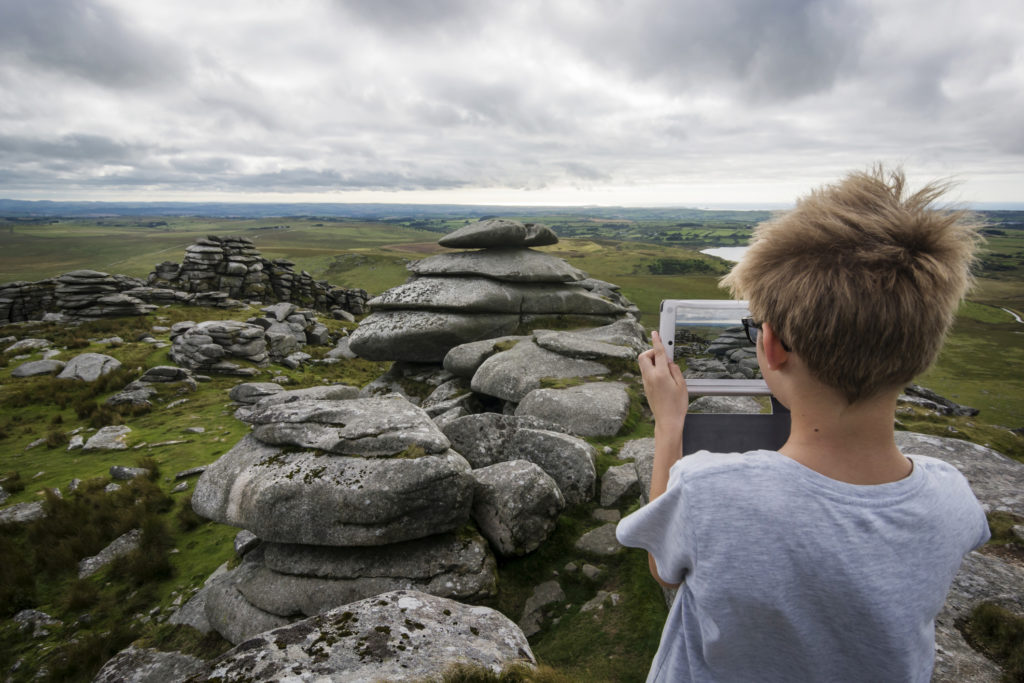 A young boy photographs a landscape in Cornwall using his tablet device