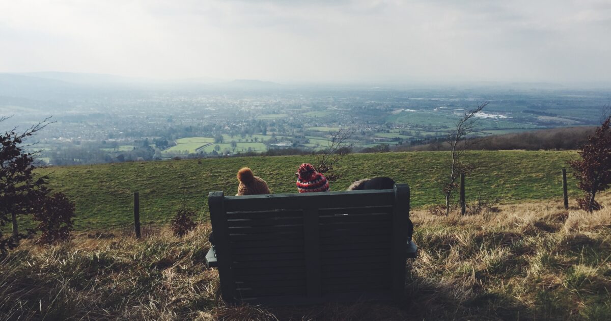 Two children sitting on a bench on top of a hill at Cleeve Hill, Cheltenham