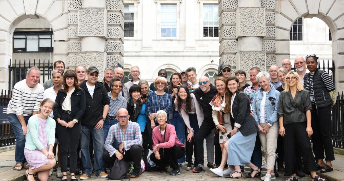 Picture shpwing a mixed group of people posing for a photograph in front of a building