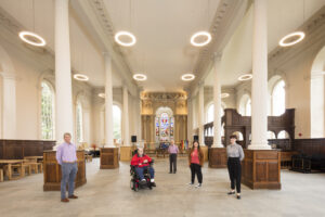 Wide angle shot of a bright room with large pillars. 5 people dotted around the the rom, socially distanced.