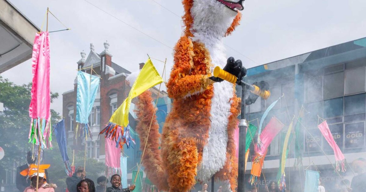 A large puppet of a fox moving along a street as part of a carnival
