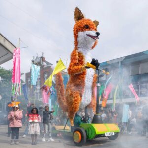 A large puppet of a fox moving along a street as part of a carnival